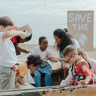 A group of students doing a beach cleanup with their teacher, with a 'save the earth' sign in the background.