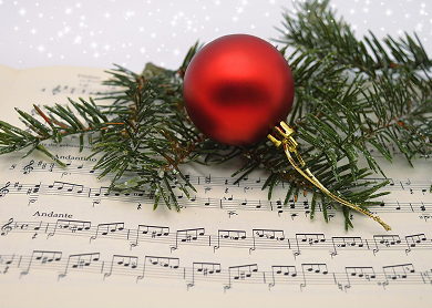 a red christmas ornament bauble with pine tree sprigs laying ontop of sheet music.