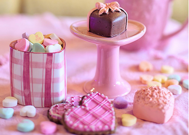conversation hearts, heart shaped iced cookies and heart shaped chocolates placed on a pink table cloth